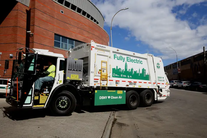 A New York City electric sanitation truck with "fully electric" on its side in green lettering.
